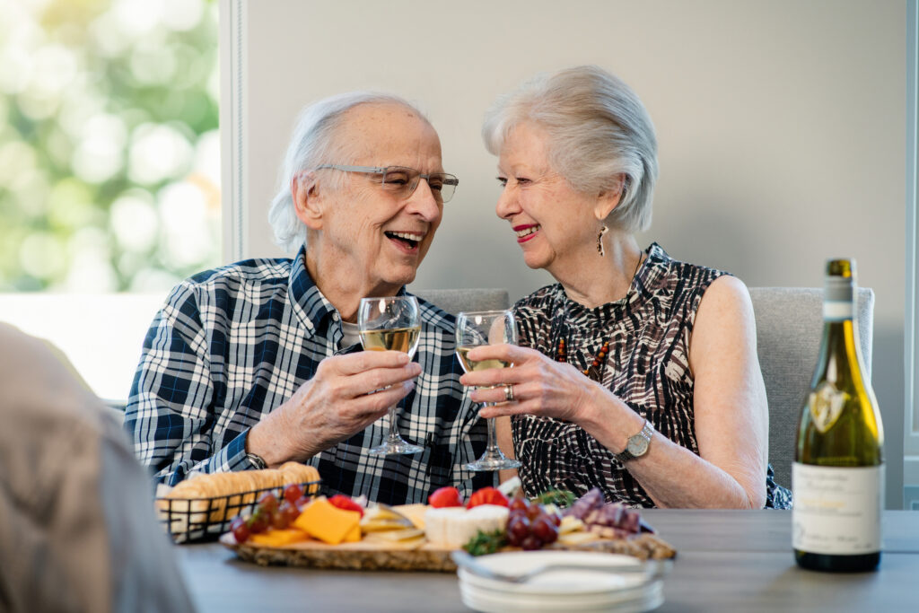 A male-female couple look into each others' eyes while holding wine glasses at a table.
