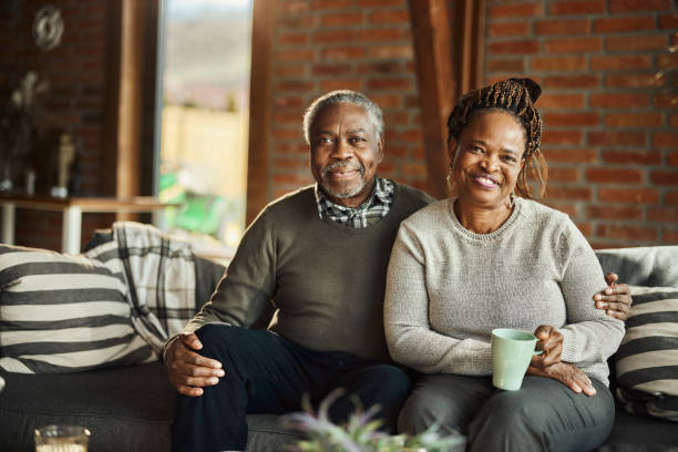 A Black senior couple sits in their living room.
